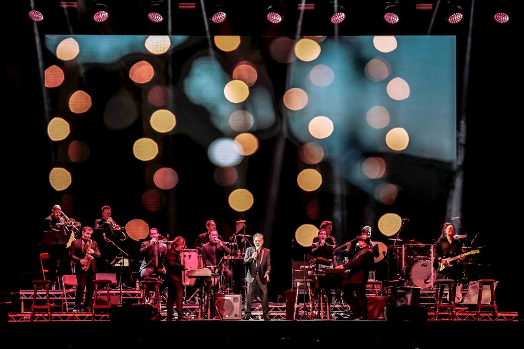 Frankie Valli with a full band onstage and bokeh background